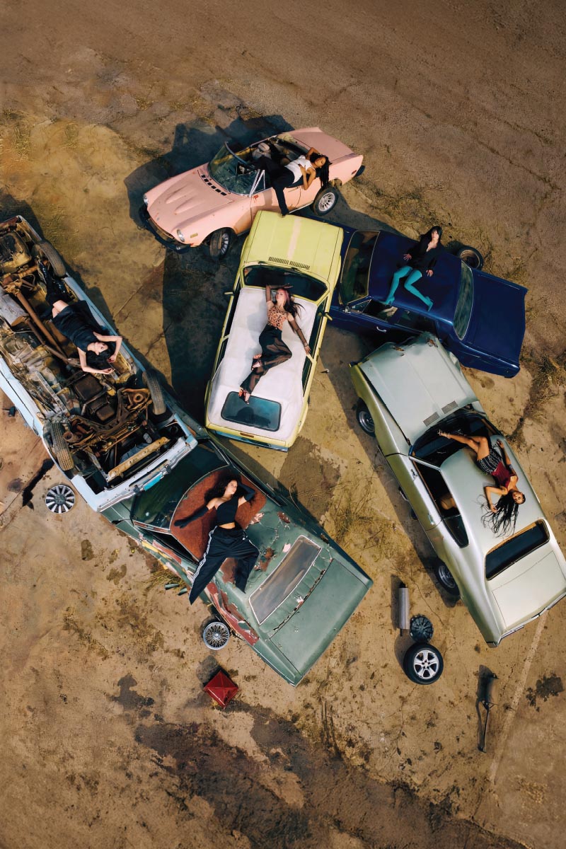 KATSEYE poster featuring the group posed around a vehicle in an overhead photograph